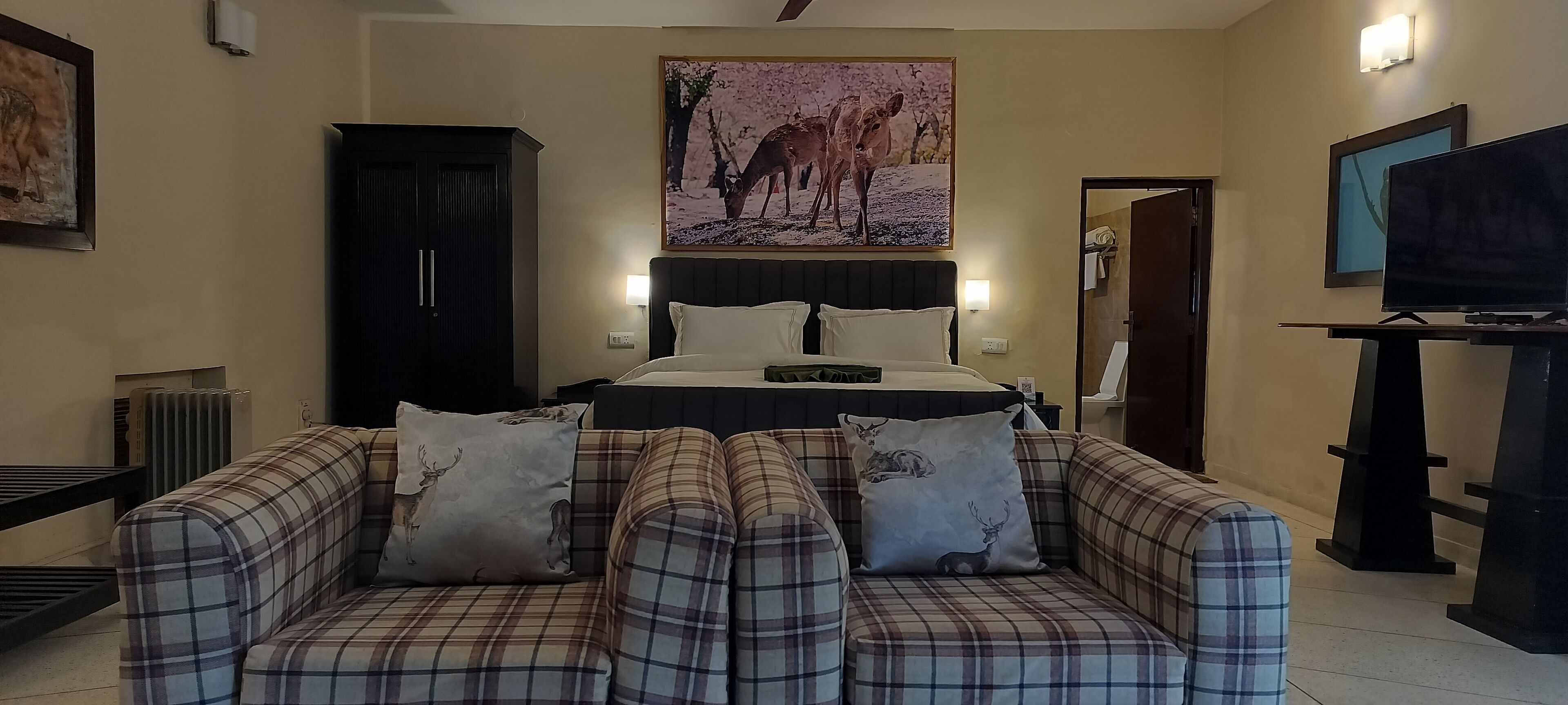 A hotel room with a bed, a sofa, a television, and a painting on the wall.