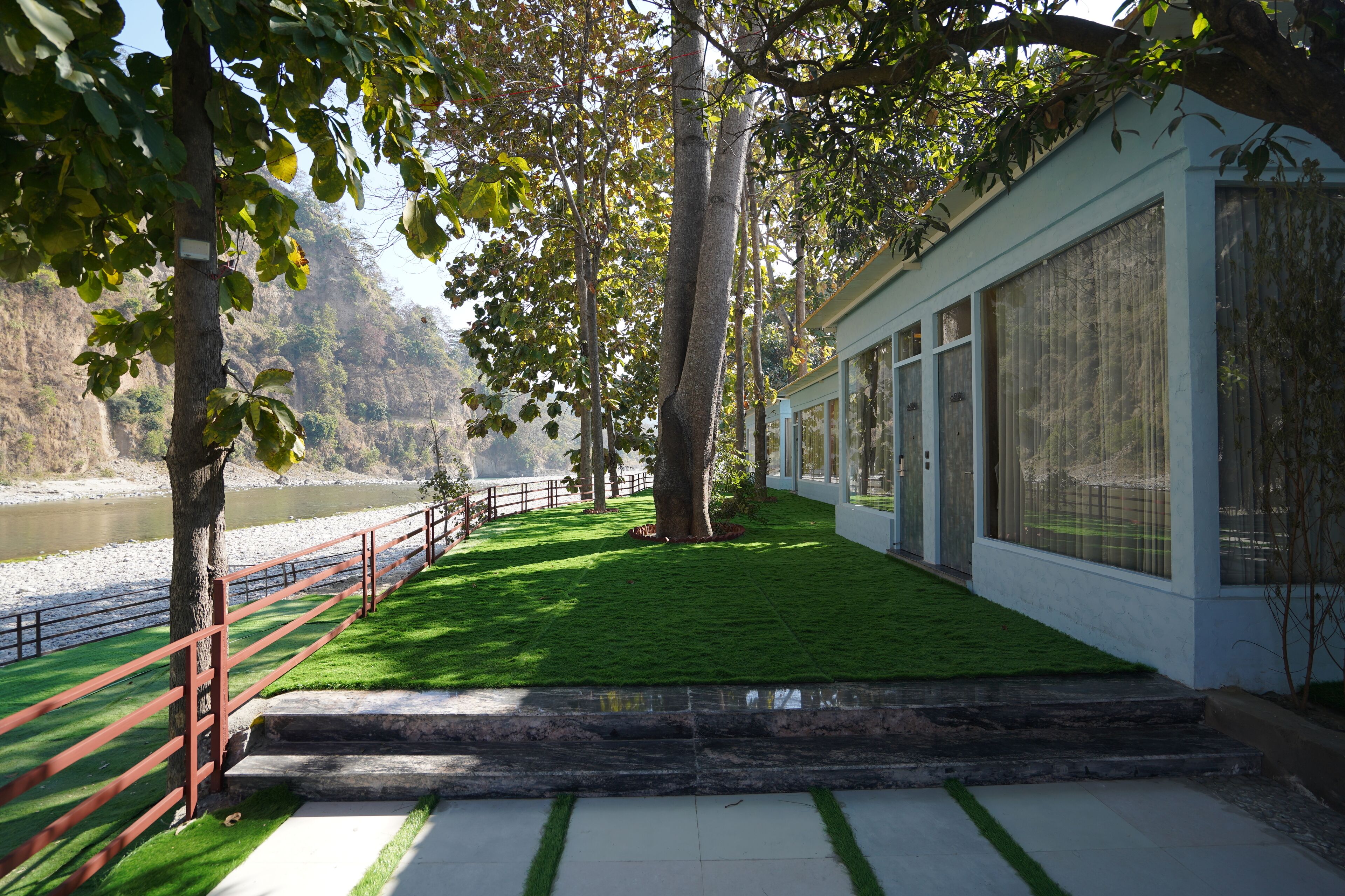 Un sendero que lleva a un edificio con amplias ventanas, un césped verde y un río al fondo.