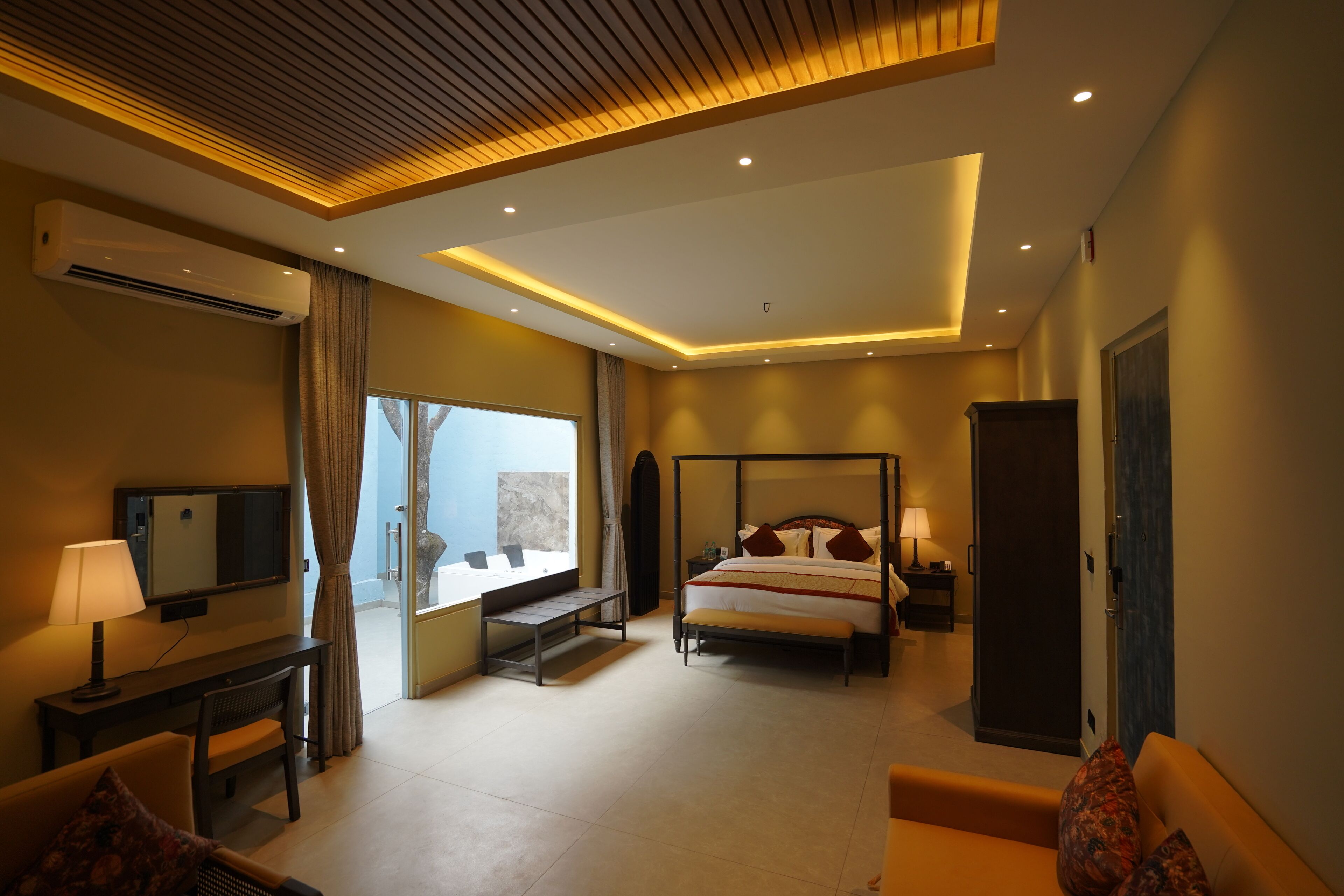 A modern hotel room with a bed, bedside table, lamp, TV, and a view of the outdoors.