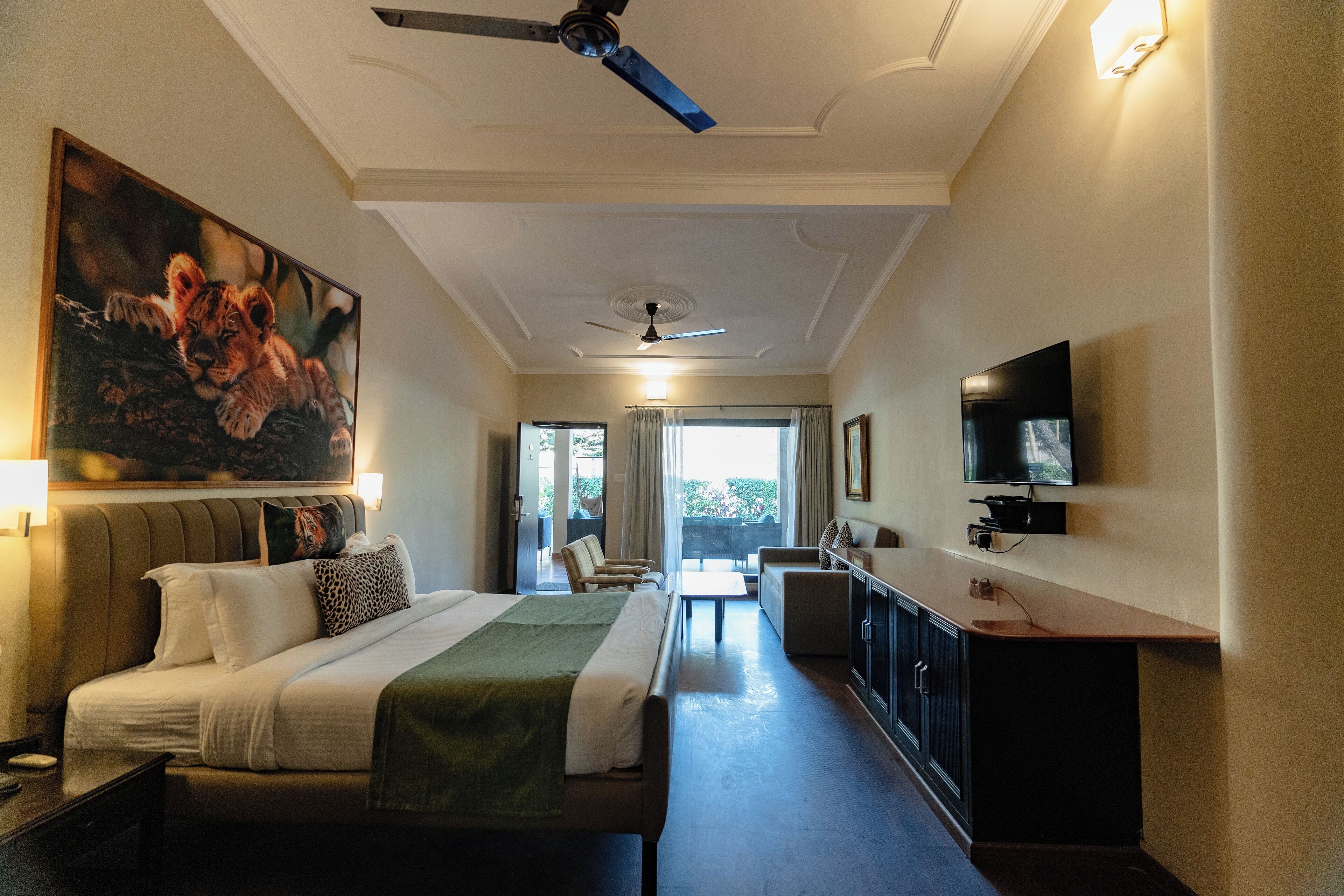 A hotel room with a bed, a desk, a chair, a television, and a painting of a lion cub.
