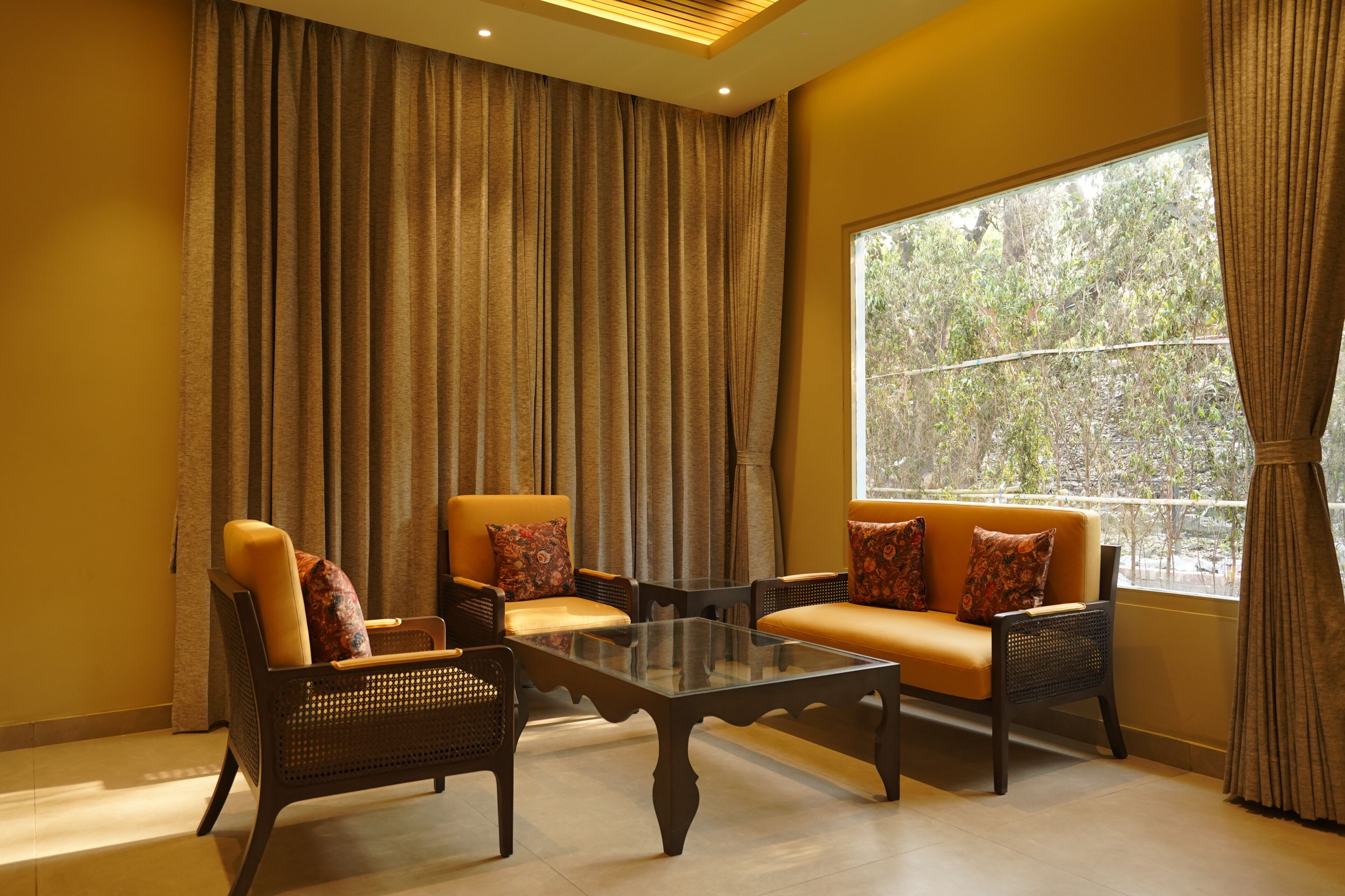 A room with a sofa set, a glass coffee table, and a large window with curtains.