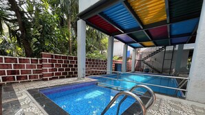 En swimmingpool med kakelbeklädda trappsteg och metallräcken, omgiven av en tegelmur och ett kaklat golv med ett geometriskt mönster.