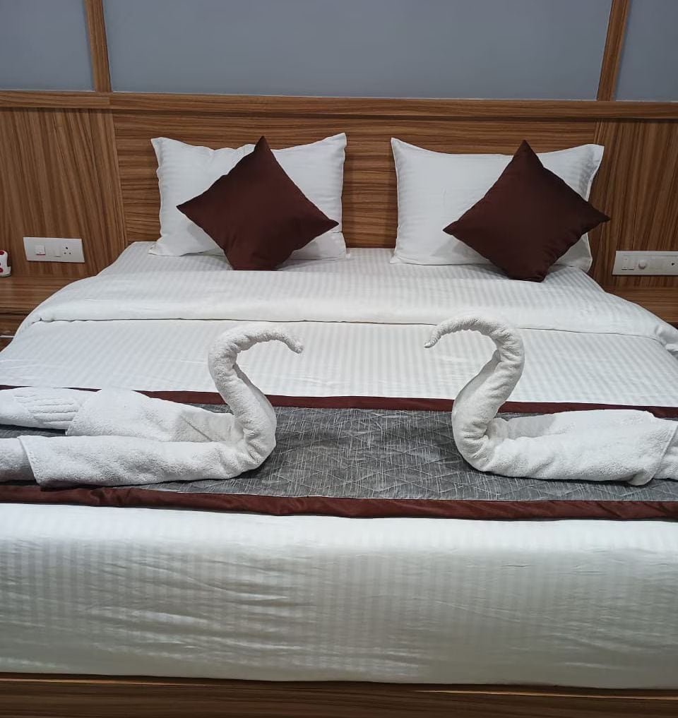 A neatly made bed with a headboard, pillows, and two towels arranged in a swan shape.