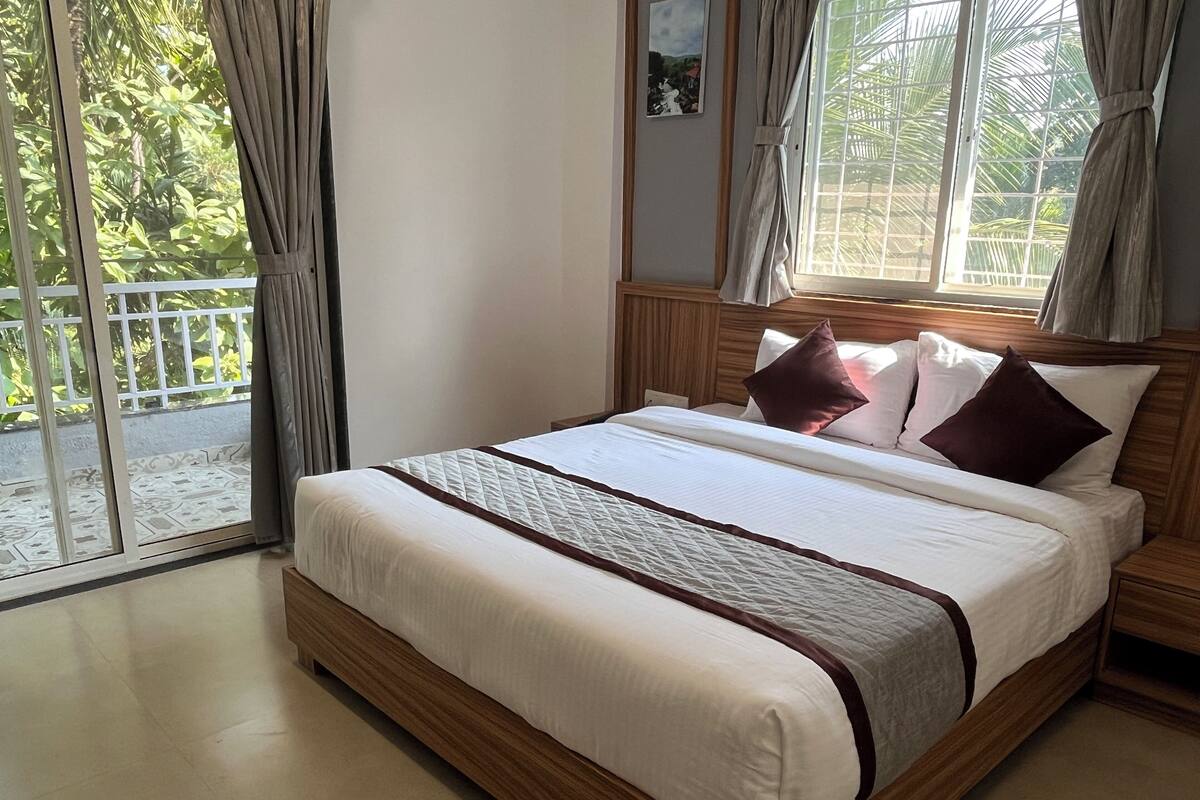 Une chambre avec un lit en bois, du linge de lit blanc et une vue sur la verdure par la fenêtre.