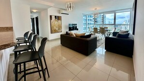 A modern living room with a dining area, large windows, and a city view. - Gold Tower - Bright 3 BDR Apt in Costa del Este (Panama City)