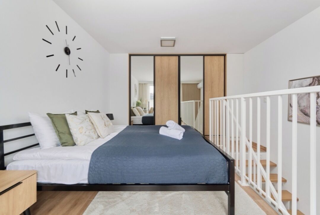 A modern bedroom with a bed, a clock, a mirror, and a staircase.