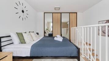 A modern bedroom with a bed, a clock, a mirror, and a staircase.