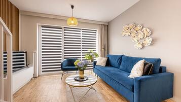Una sala de estar moderna con un sofá azul, una mesa de centro redonda y un ventanal con persianas.