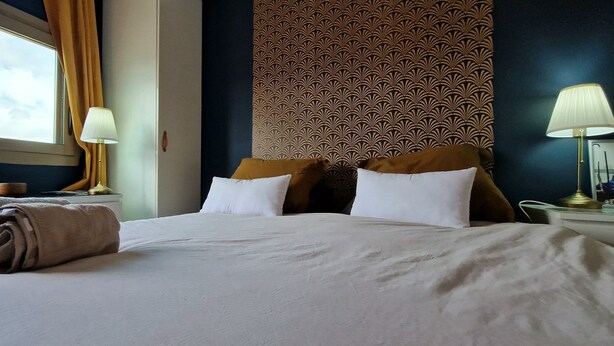 A hotel room with a bed, two bedside lamps, a window with curtains, and a patterned wall. - "BlueSky" air-conditioning-wi-fi garage- 5m from town center.  (Aix-en-Provence)