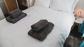 A neatly made bed with white bedding and two folded gray towels on the side.