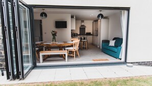 A modern open-plan living and dining area with a kitchen, a teal sofa, and a dining table set for four.