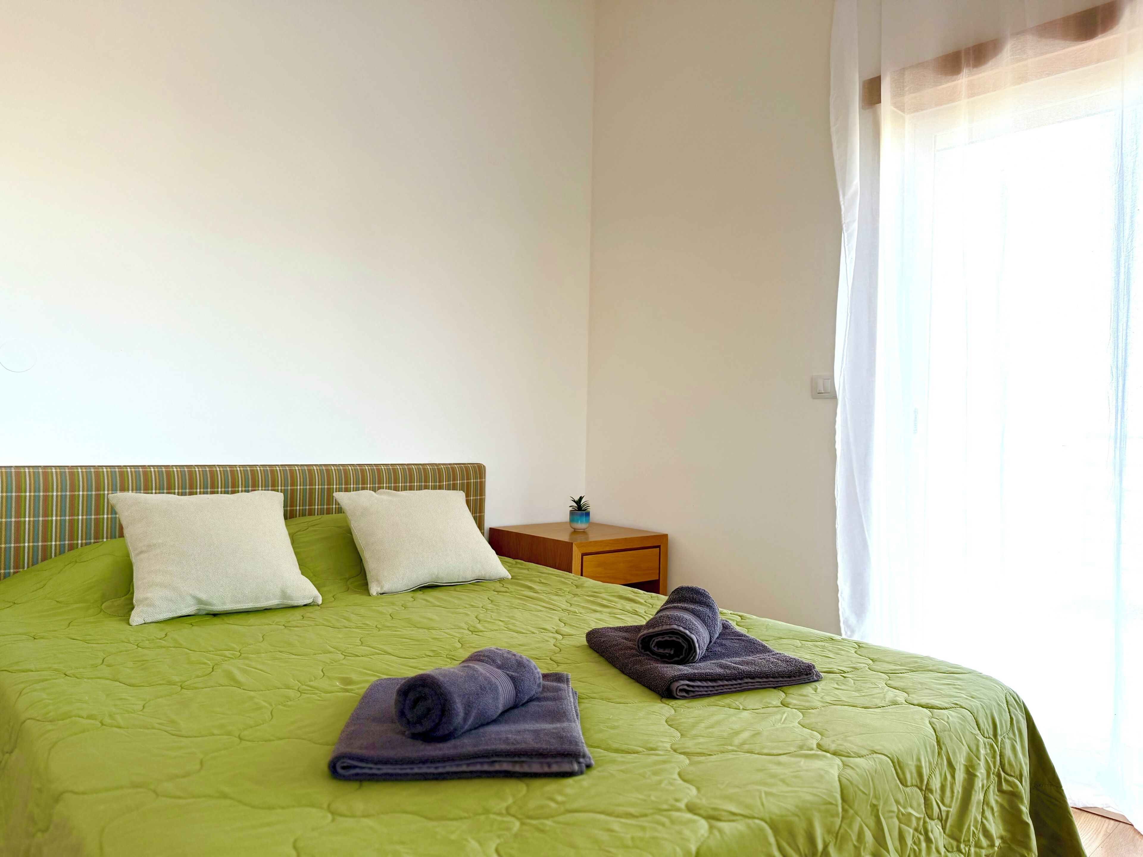 A bed with a green quilt, two pillows, and two folded towels.