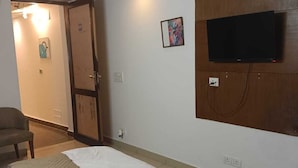 Habitación de hotel con una cama, televisión montada en la pared, ventilador de techo y una puerta que da a otra habitación.