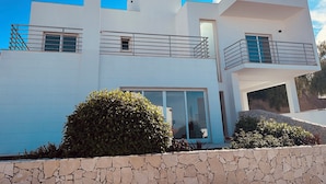 Una casa moderna de dos pisos con fachada de piedra, ventanas grandes y un balcón con barandillas de metal.