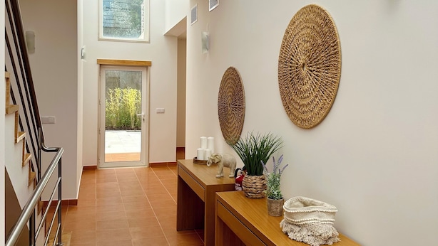Un pasillo amplio con un banco de madera, una mesita con objetos decorativos y vistas a una puerta que da al exterior.