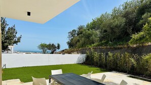 Un patio exterior con mesa y sillas, un césped y vistas al mar.