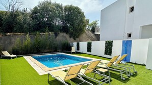 Una piscina con césped artificial, sillas de descanso y un edificio blanco al fondo.