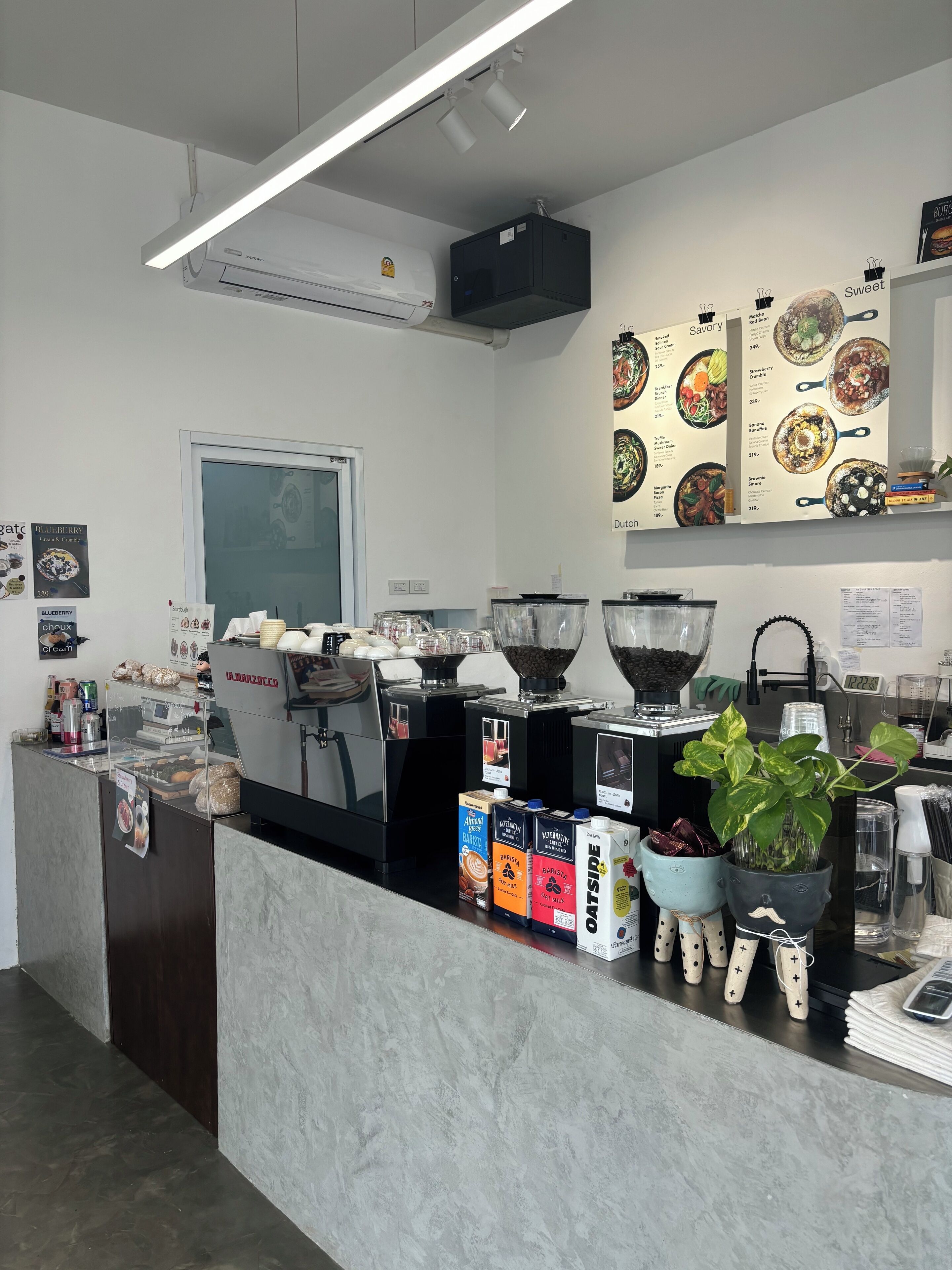Interior de una cafetería con una máquina de café, carteles de menú y varios recipientes para café.
