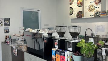 Interior de una cafetería con una máquina de café, carteles de menú y varios recipientes para café.