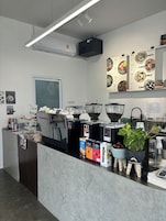 Interior de una cafetería con una máquina de café, carteles de menú y varios recipientes para café.