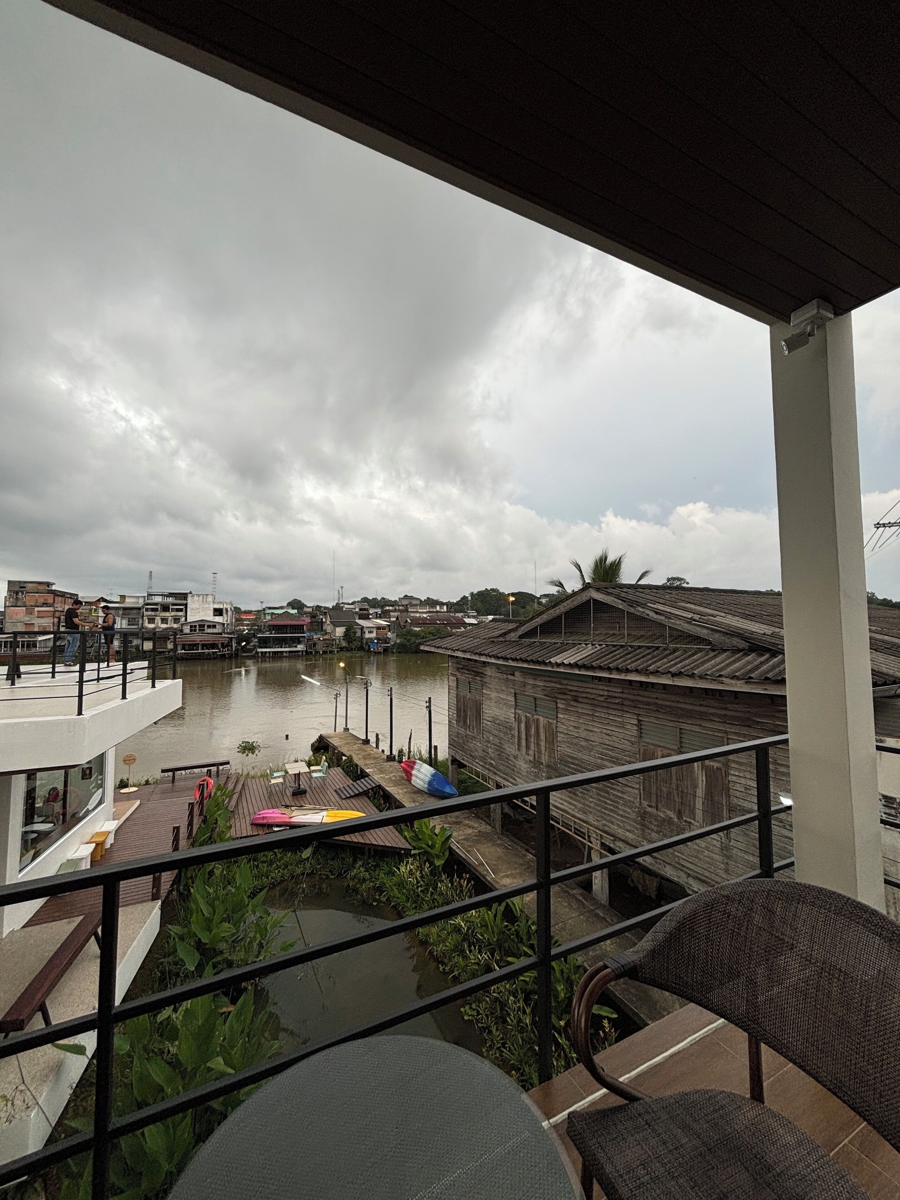A balcony overlooking a river with traditional buildings, a wooden dock, and a modern building with a glass facade.
