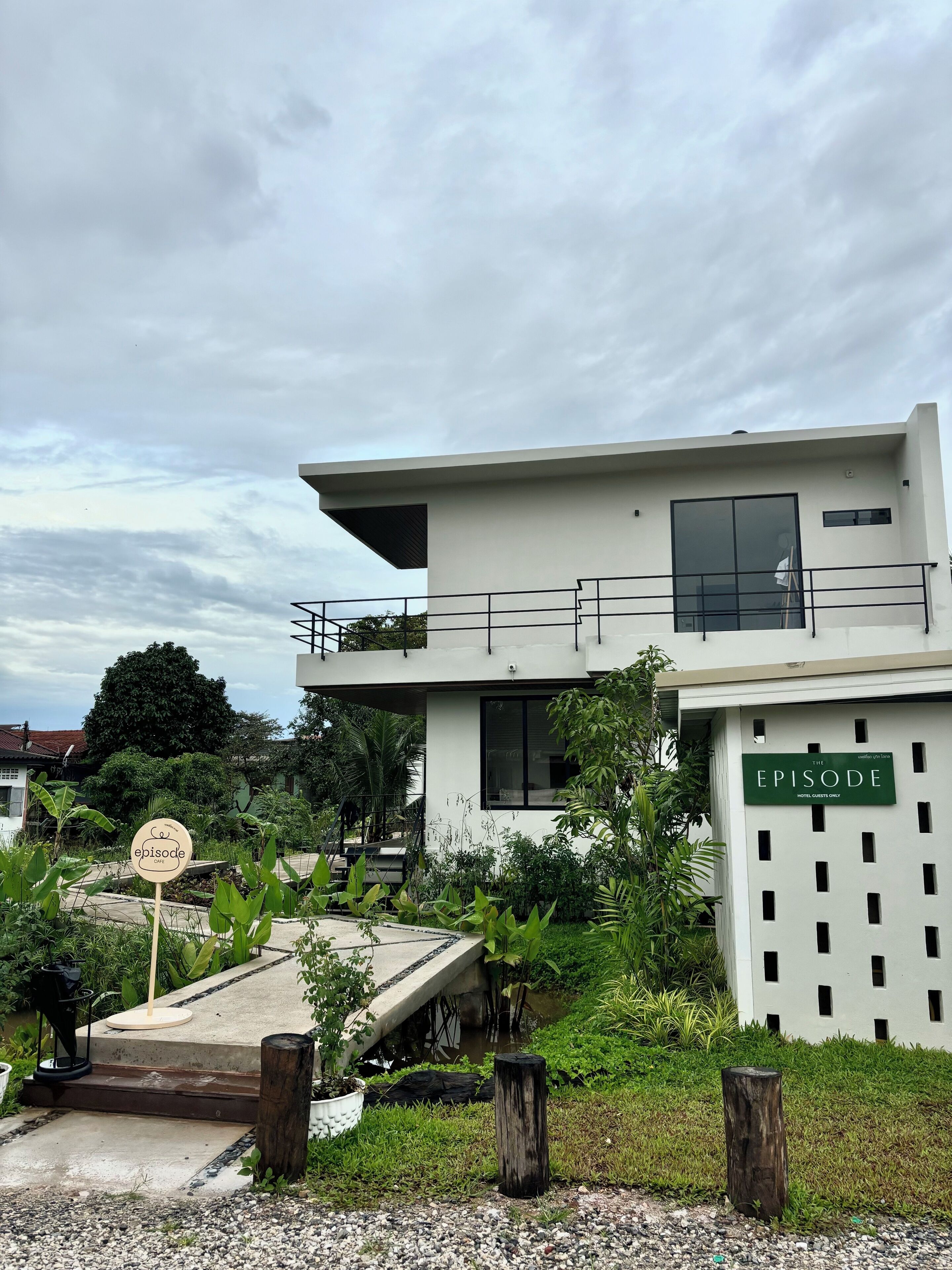 Un bâtiment moderne à deux étages, doté d’un balcon, d’une enseigne indiquant qu’il s’agit d’un hôtel, et d’une végétation luxuriante au premier plan.
