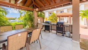 En uteplats med ett takförsett sittområde, en grill och utsikt över en byggnad i bakgrunden.