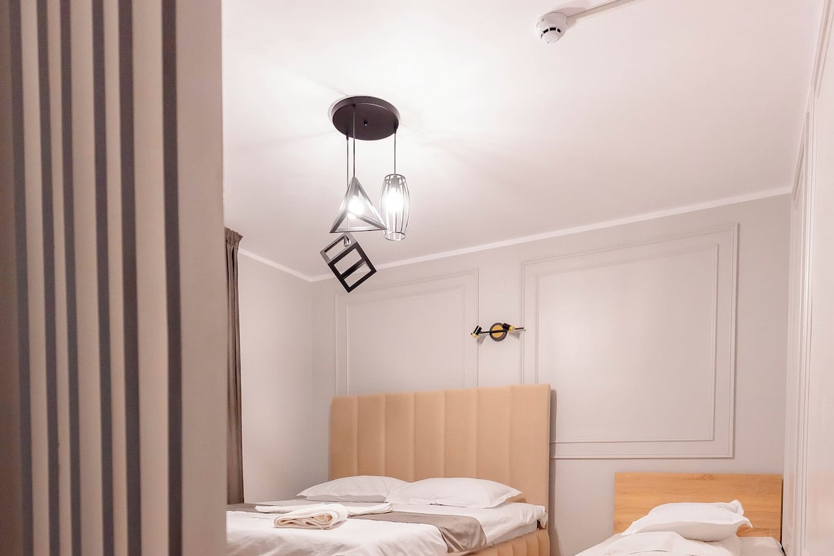 A bedroom with two beds, wooden flooring, and a ceiling light fixture.