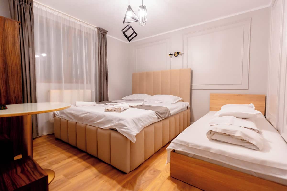 A hotel room with a large bed, a smaller bed, a wooden table, and a hanging light fixture.