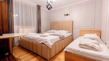 Een hotelkamer met een groot bed, een kleiner bed, een houten tafel en een hangende lamp.
