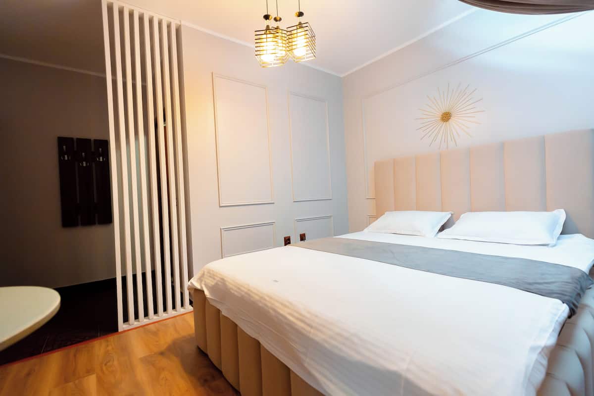A modern bedroom with a large bed, a bedside table, a wall-mounted light fixture, and a decorative wall piece.