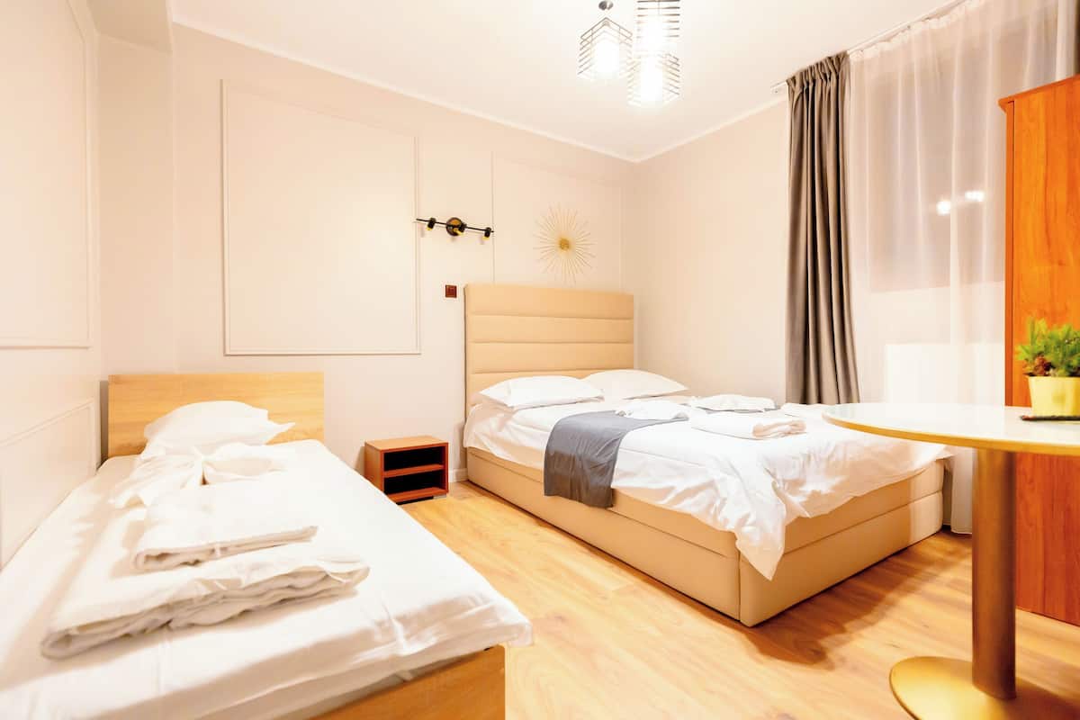 A hotel room with a bed, a bedside table, a small nightstand, and a window with curtains.