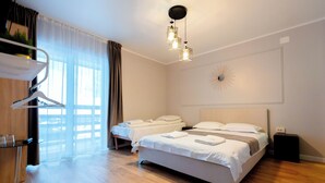 A modern hotel room with two beds, a wooden floor, a desk with a chair, a hanging light fixture, and a decorative wall piece. - Complex Veverita  (Novaci)