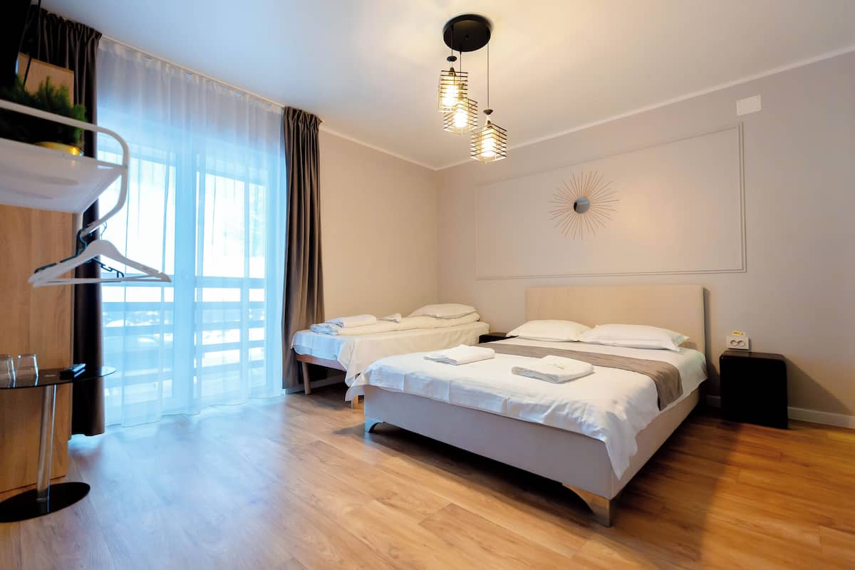 A modern hotel room with two beds, a wooden floor, a desk with a chair, a hanging light fixture, and a decorative wall piece.