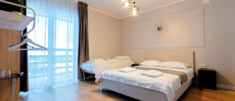 A modern hotel room with two beds, a wooden floor, a desk with a chair, a hanging light fixture, and a decorative wall piece.