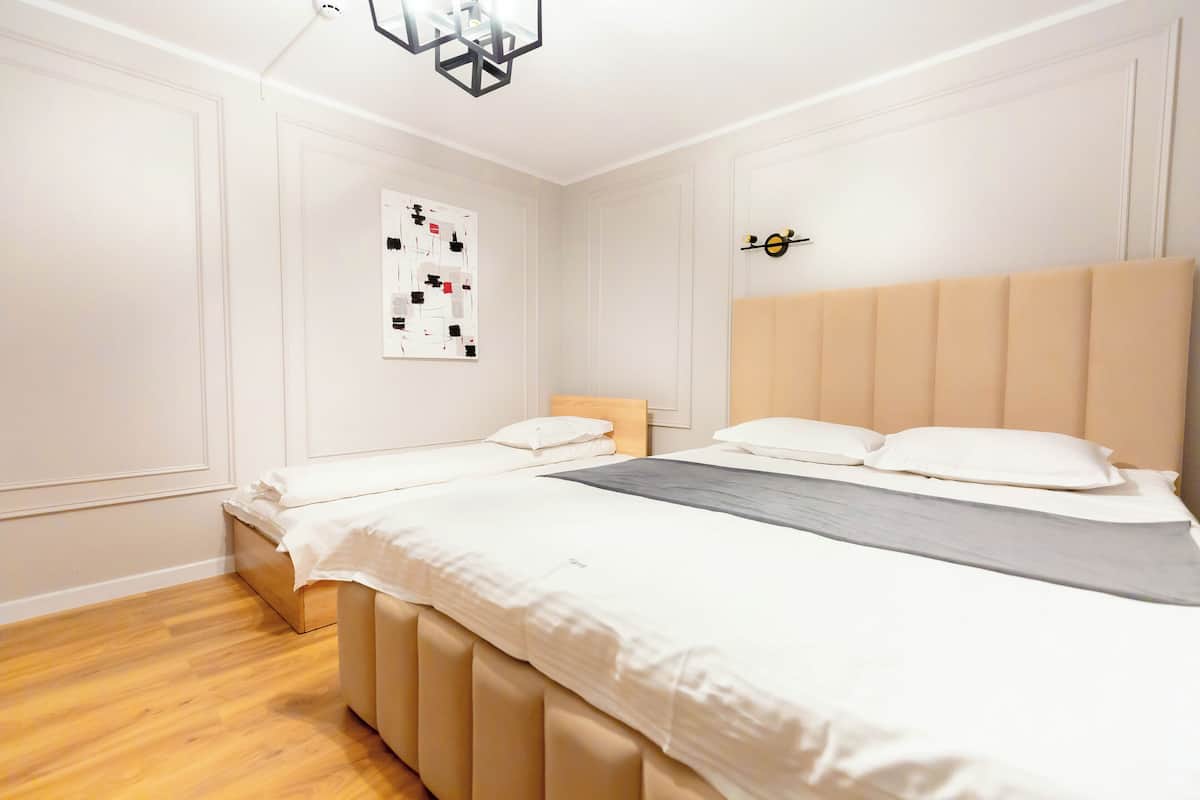 A bedroom with a large bed, a bedside table, a wall-mounted clock, and a framed abstract artwork.