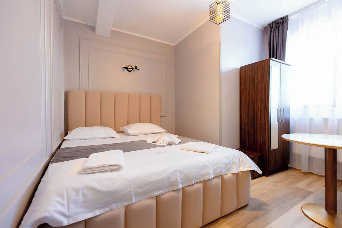 A neatly made bed with a headboard, a wooden wardrobe, and a round table in a hotel room.