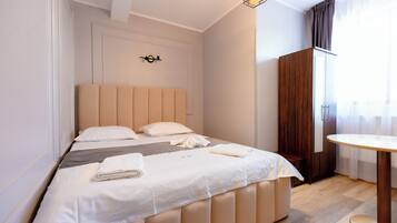 A neatly made bed with a headboard, a wooden wardrobe, and a round table in a hotel room.