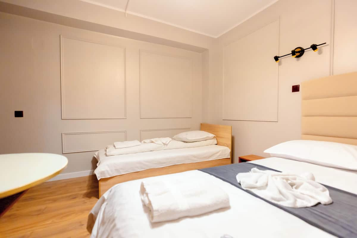 A hotel room with a bed, a bedside table, a wooden headboard, and a wall-mounted light fixture.