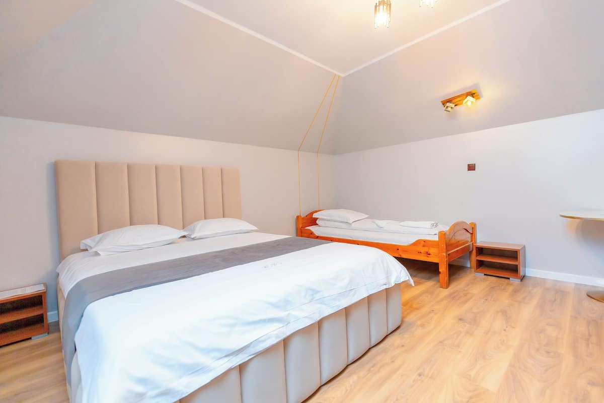 A bedroom with a large bed, a smaller bed, a bedside table, and a wall-mounted shelf.