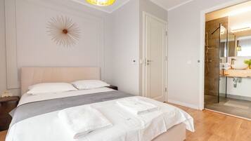 Una habitación de hotel moderna con una cama grande, una mesita de noche, un aplique en la pared y un baño visible a través de una puerta abierta.