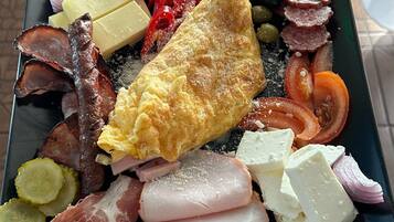 A plate of food with an omelette, various meats, cheese, and vegetables.