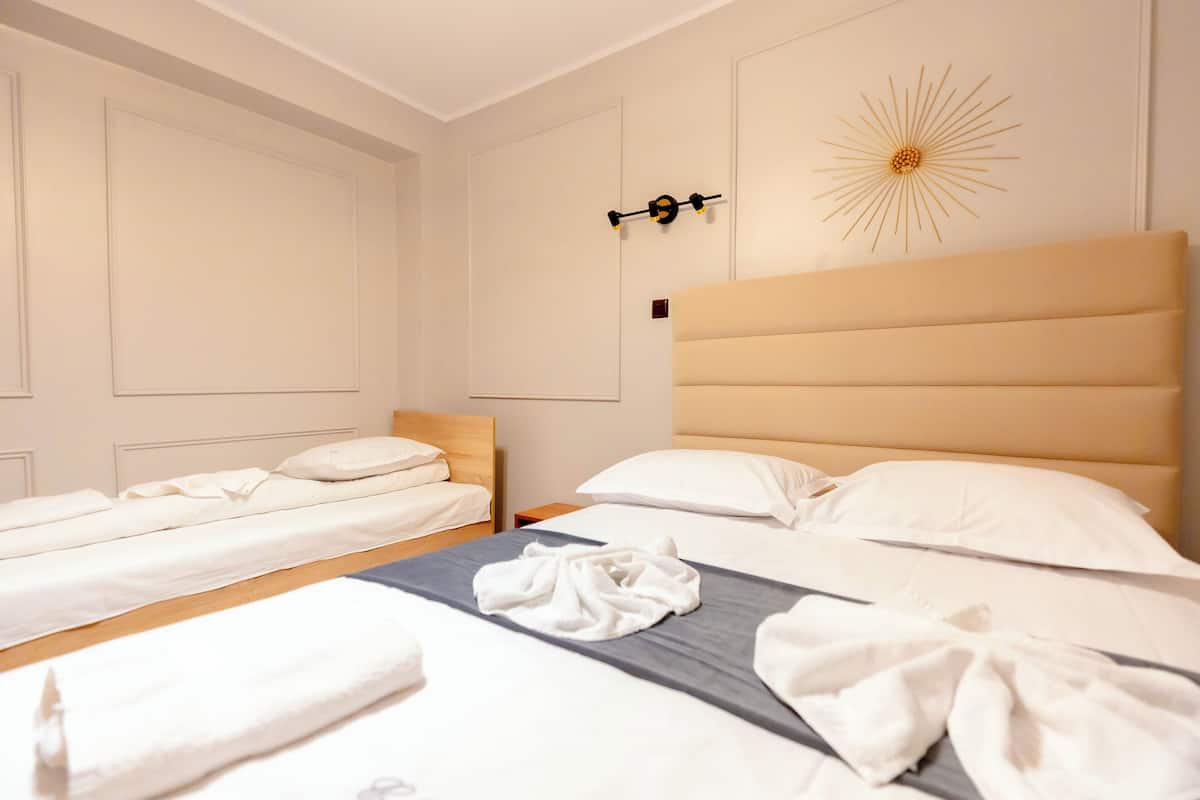 A hotel room with two single beds, a larger bed, and a headboard.