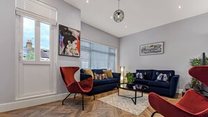 Ein modernes Wohnzimmer mit einem blauen Sofa, roten Sesseln, einem Holzboden mit Fischgrätmuster und Kunstwerken an den Wänden.