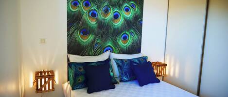 A bedroom with a bed, peacock-themed wall tapestry, and two bedside tables with lamps.