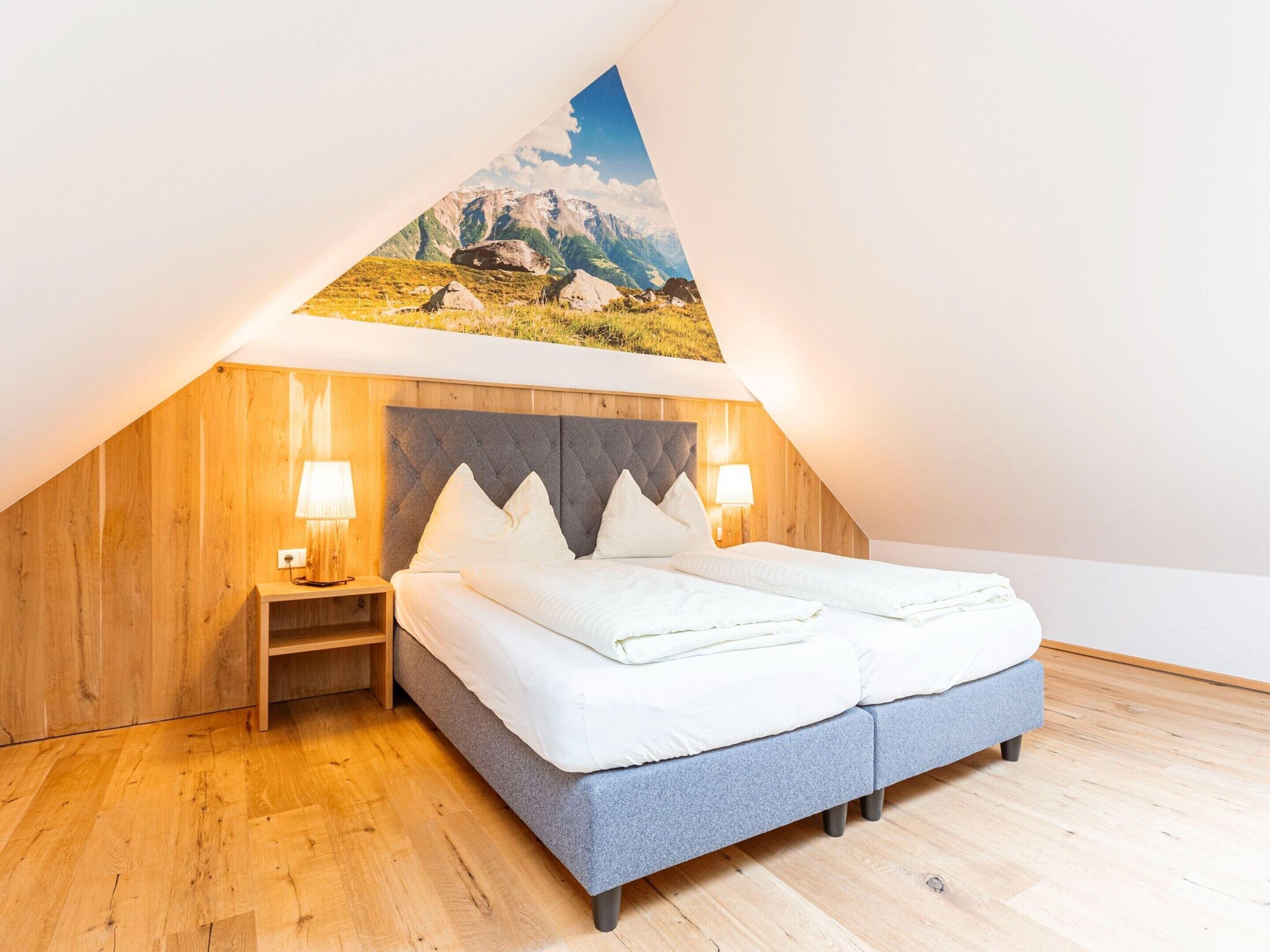 Un dormitorio con techo inclinado, una cama con ropa de cama blanca, dos lámparas de noche y un cabecero de madera.