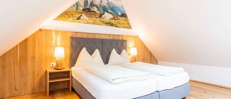 Un dormitorio con techo inclinado, una cama con ropa de cama blanca, dos lámparas de noche y un cabecero de madera.