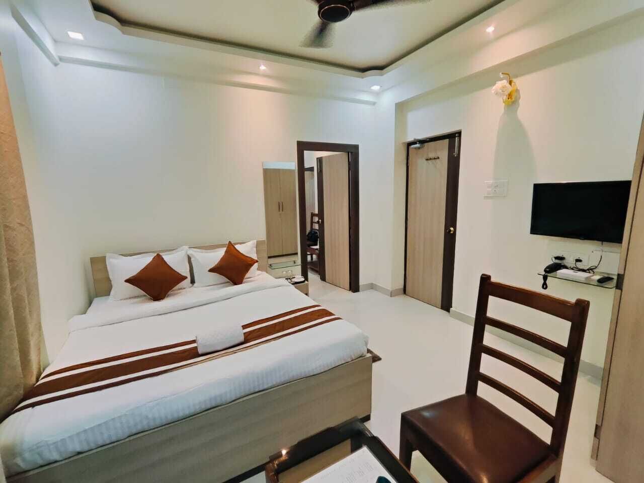Quarto de hotel com cama, cadeira, televisão e guarda-roupa.