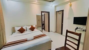 Quarto de hotel com cama, cadeira, televisão e guarda-roupa.