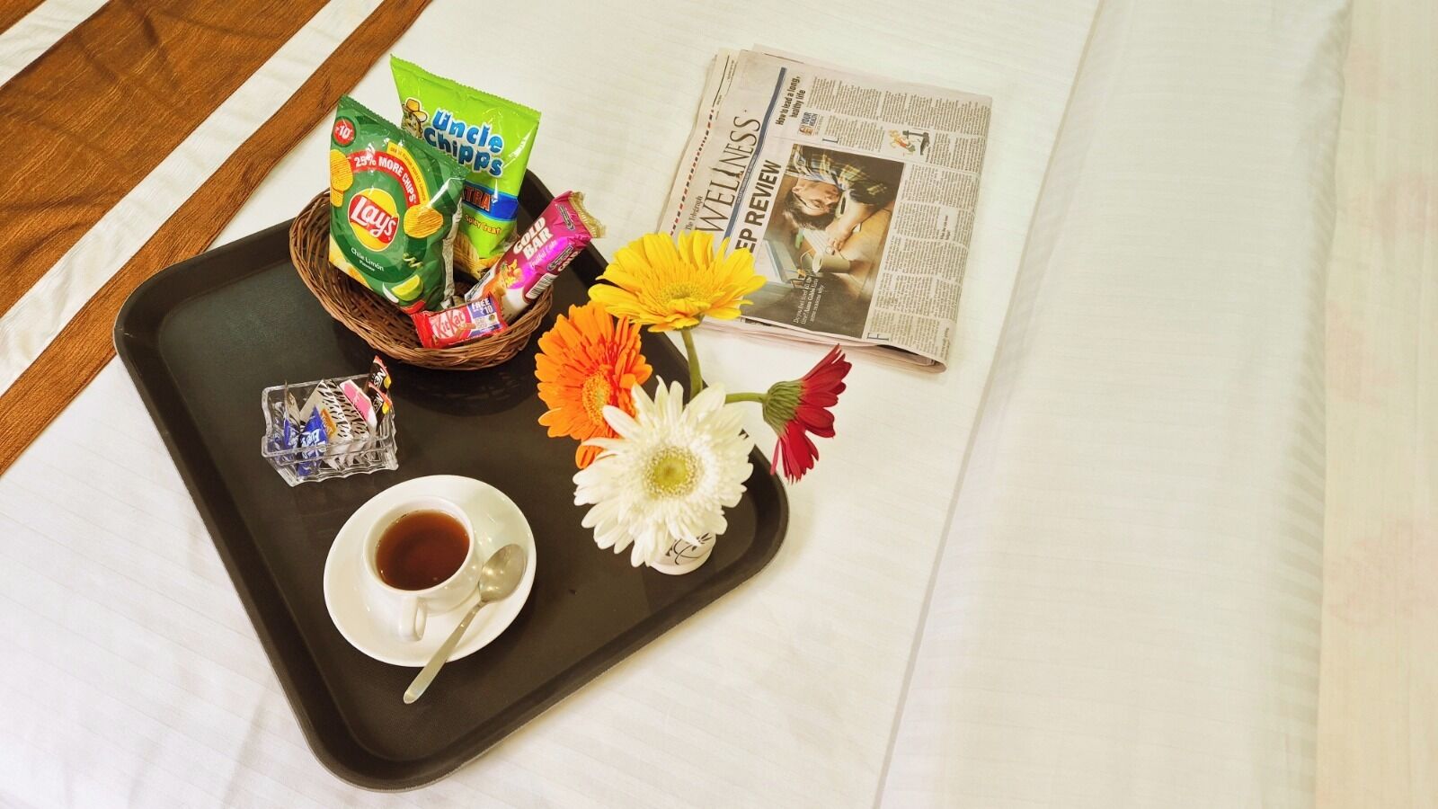 A tray with snacks, a cup of tea, and flowers on a bed.